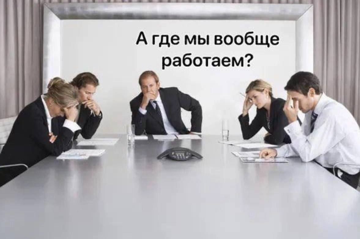 А где мы вообще работаем? Пять человек в деловых костюмах сидят за столом, подперев головы руками, на экране сзади надпись: «А где мы вообще работаем?»