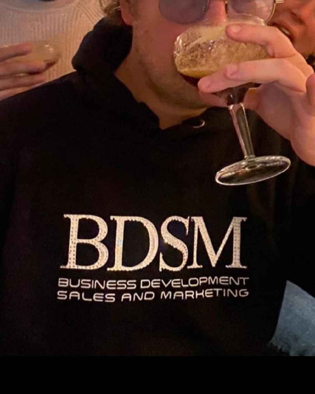 BDSM Business Development Sales and Marketing Человек пьет пиво в худи с аббревиатурой BDSM, которая расшифровывается как Business Development Sales and Marketing