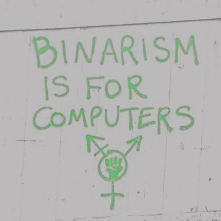 Надпись на стене: «Binarism is for computers» и символ в стиле трансгендерного знака с кулаком.