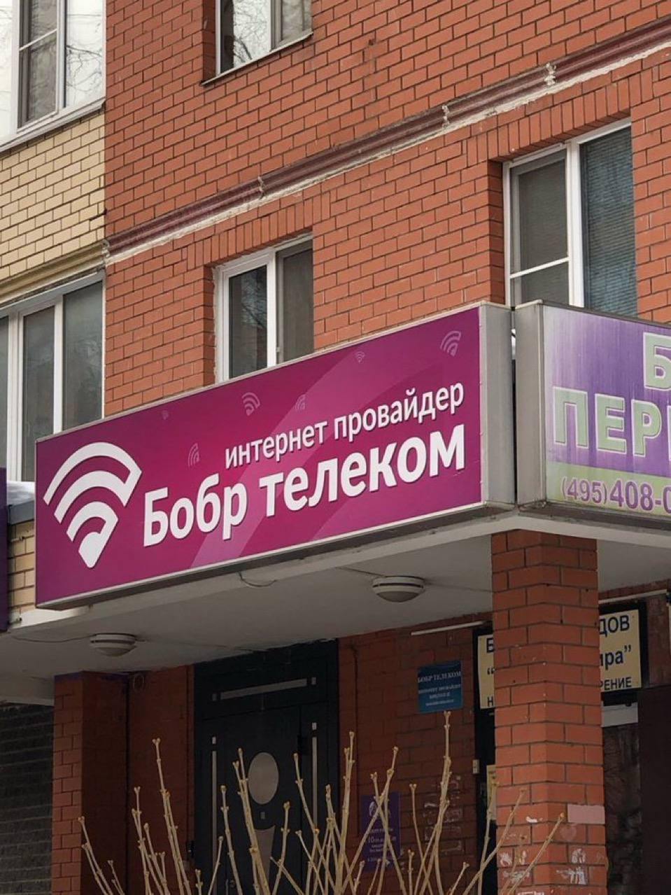 Бобр телеком Мем с вывеской интернет-провайдера «Бобр Телеком» и символом Wi-Fi, на фоне кирпичного здания.