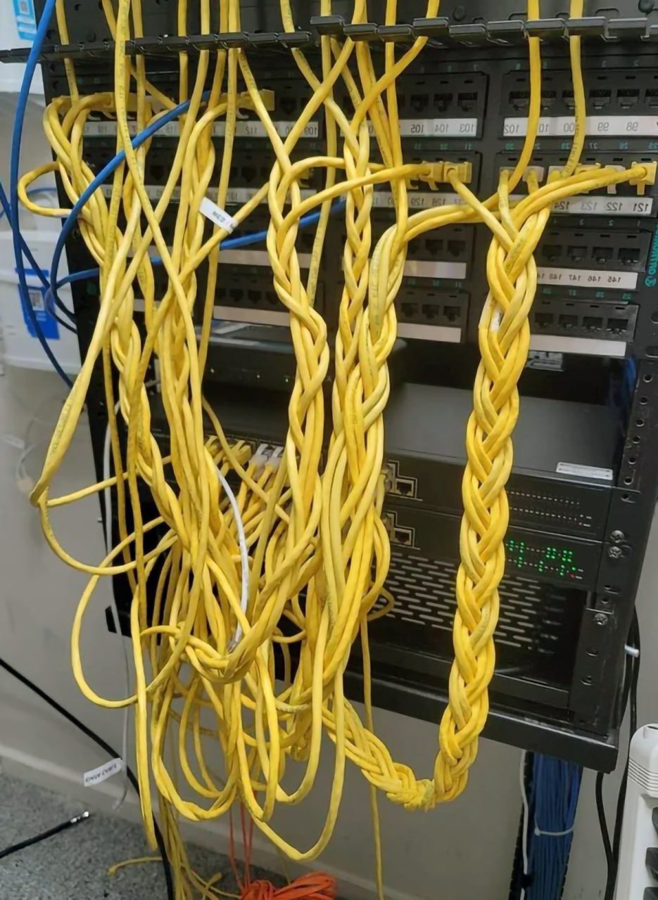 Плетеные кабели Ethernet Множество желтых кабелей Ethernet, часть из которых запутана, а часть аккуратно заплетена в косу, свисающую с серверной стойки.