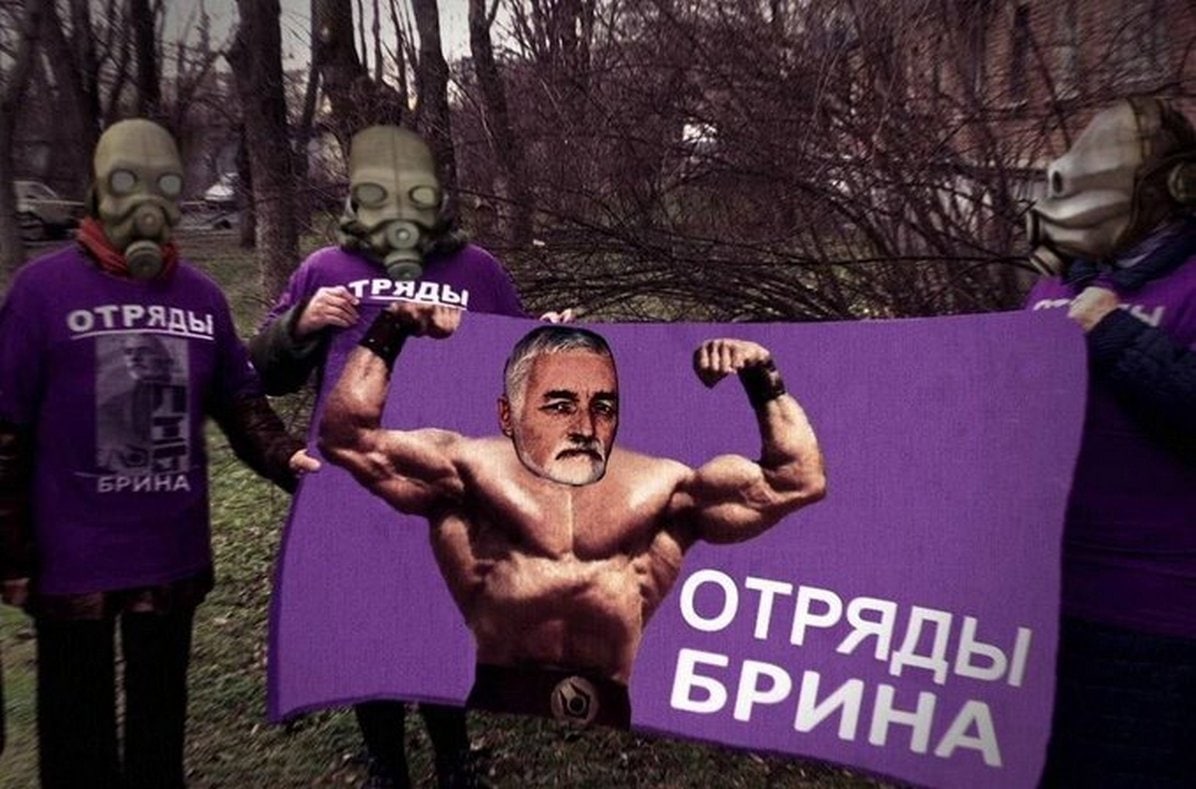 Отряды Брина Мем, изображающий троих людей в противогазах с фиолетовыми футболками и плакатом «Отряды Брина» с изображением накачанного человека с лицом Брина