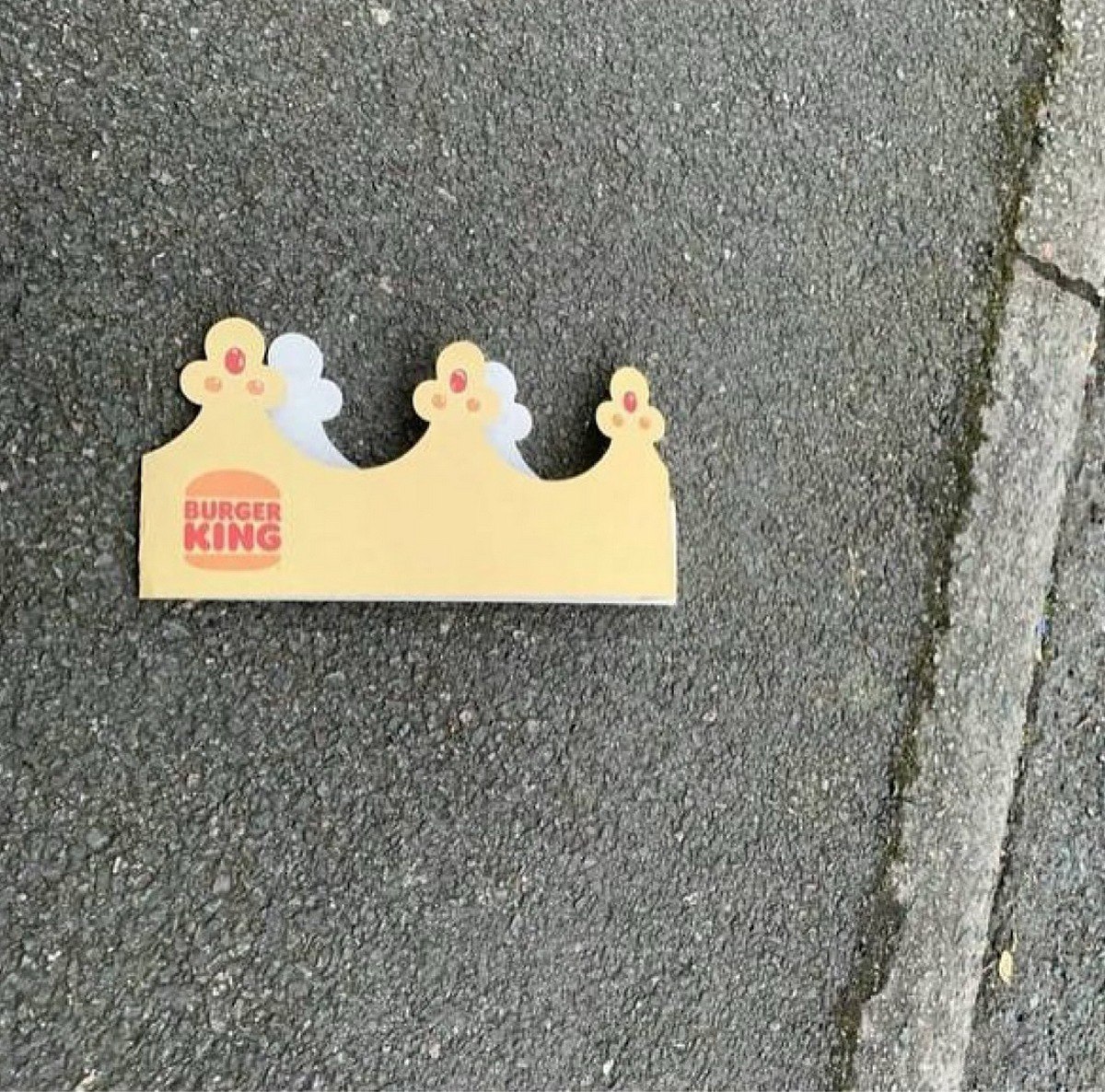 Корона Burger King на асфальте Бумажная корона "Бургер Кинг", лежащая на сером асфальте