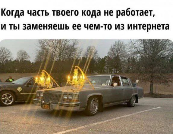 Машина с люстрами вместо фар Старый серый автомобиль с установленными на крыше хрустальными люстрами, на фоне деревьев и другой машины.