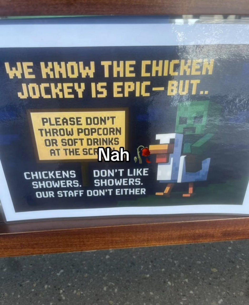Chicken jockey is epic – but nah Табличка Minecraft с надписью «WE KNOW THE CHICKEN JOCKEY IS EPIC – BUT...» и «Nah» с красной розой, призывающая не кидать попкорн и напитки в экран, потому что «курицы не любят душ, и наш персонал тоже»