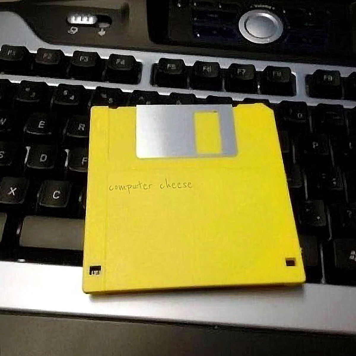 Computer cheese Желтая дискета с надписью «computer cheese» лежит на черной клавиатуре ноутбука