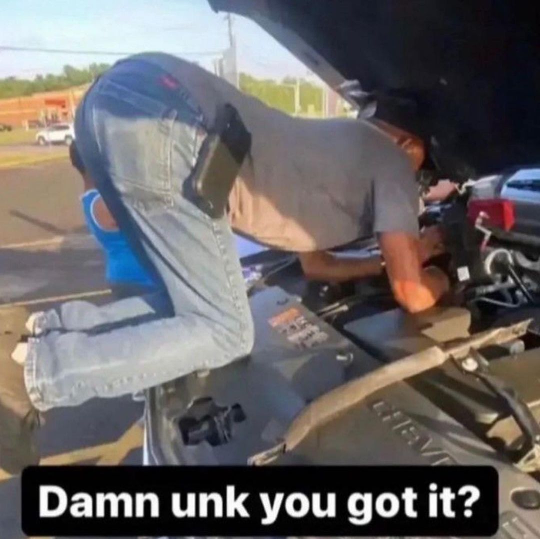 Damn unk you got it Мужчина в джинсах и футболке склонился над открытым капотом автомобиля. Его поза выглядит нелепо, а на его заднице висит кобура.