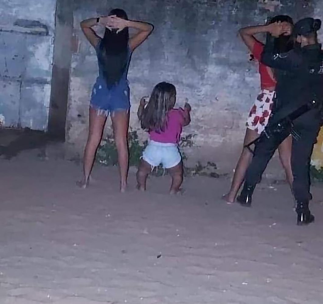 Задержание с ребенком Фотография, на которой запечатлено задержание трех девушек и ребенка, стоящих у стены, где они закрывают лица руками, а рядом с ними стоит полицейский.