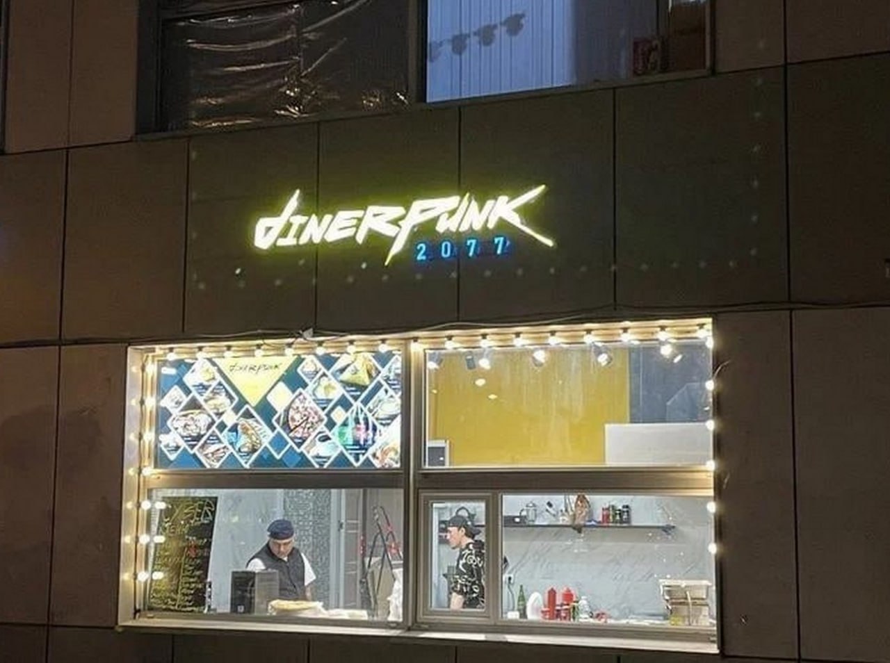 Dinerpunk 2077 Вывеска "Dinerpunk 2077" на фасаде здания, стилизованная под логотип игры Cyberpunk 2077
