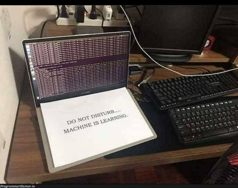 Do not disturb. Machine is learning Ноутбук с надписью «Не беспокоить, машина обучается» на столе с монитором и клавиатурами