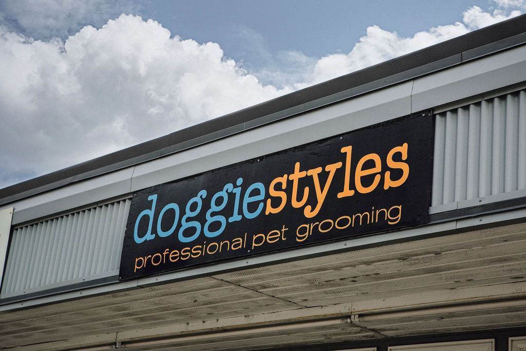 Вывеска Doggiestyles Наружная вывеска зоосалона с надписью «Doggiestyles professional pet grooming» на черном фоне, сине-оранжевыми буквами
