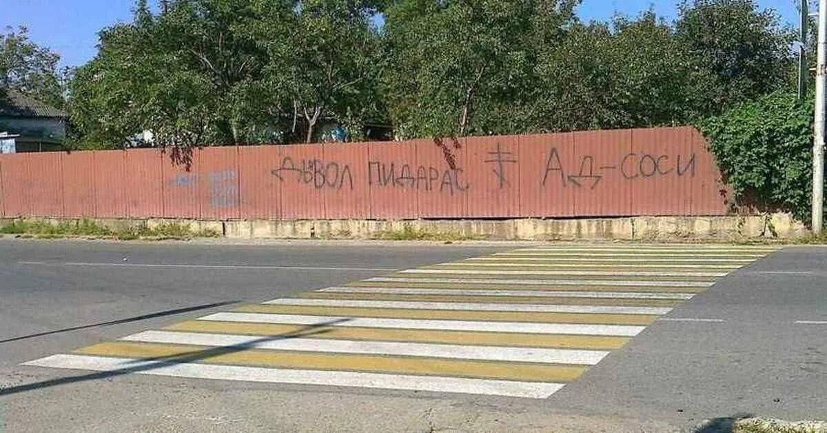 Дьявол пидарас и Ад-соси на заборе Забор с надписью "Дьявол пидарас" и "Ад-соси" на фоне пешеходного перехода