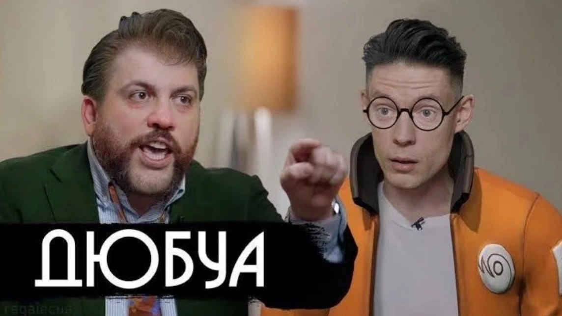 Двое мужчин в кадре: слева человек в зеленом пиджаке указывает пальцем, справа удивленный мужчина в оранжевой куртке с надписью «ДЮБА».