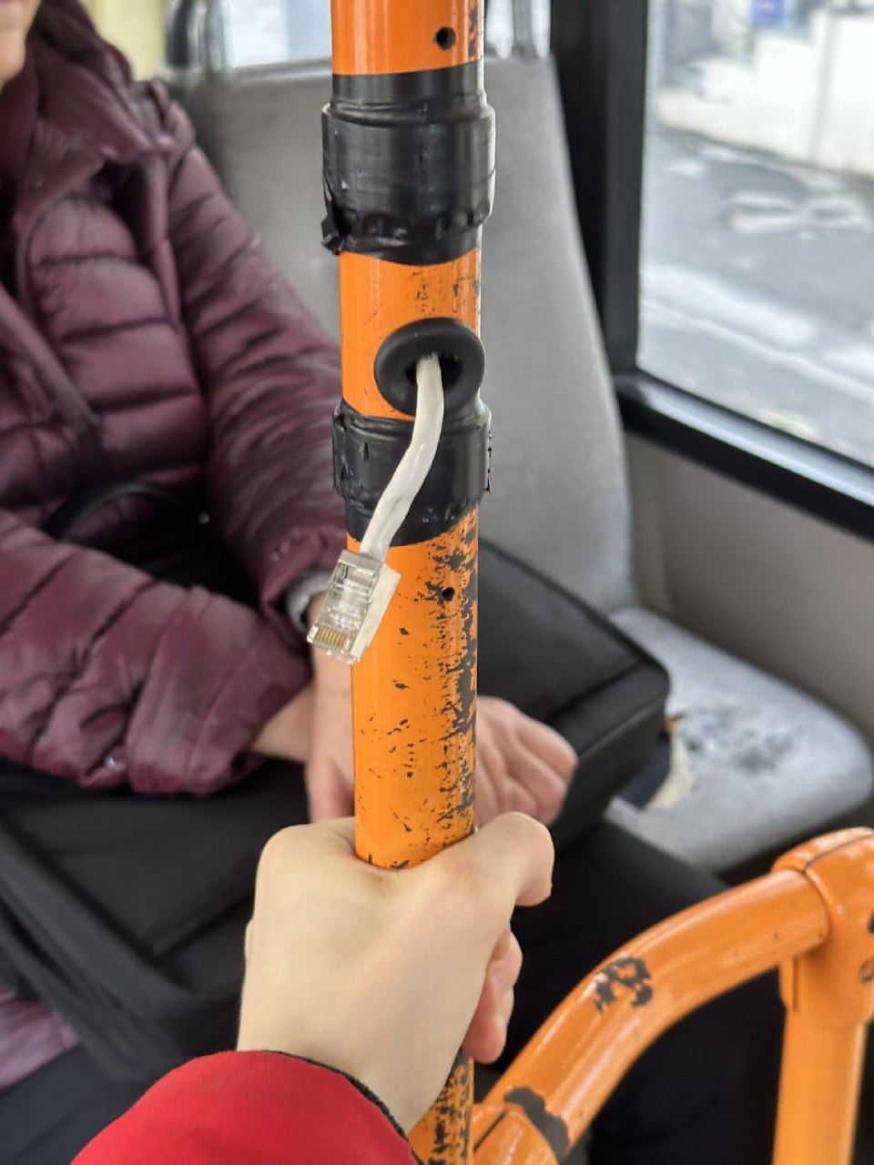 Сетевой кабель в поручне автобуса Сетевой кабель с разъемом RJ-45, торчащий из поручня в автобусе, который держит человек в красной куртке.