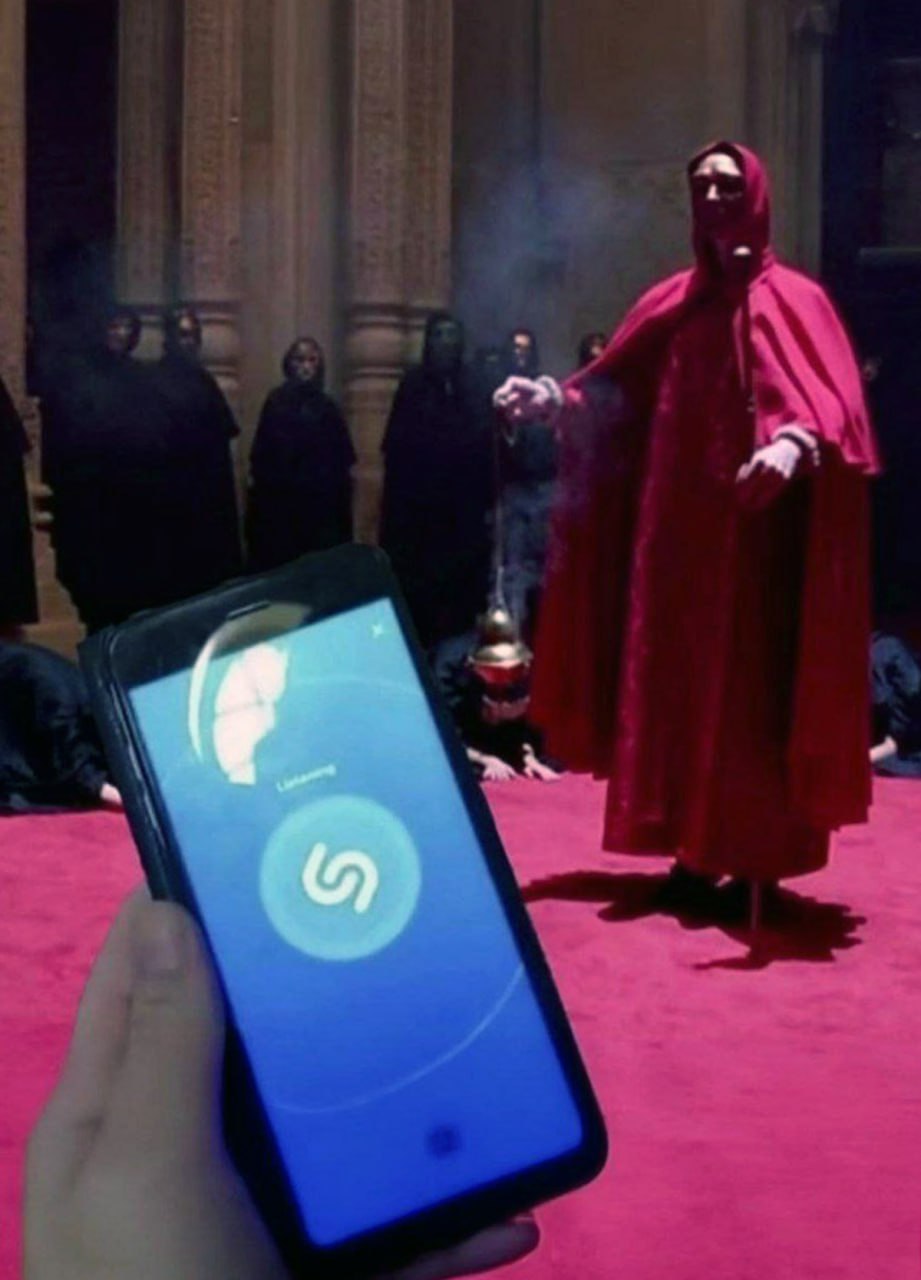 С широко закрытыми глазами Shazam Человек в красном капюшоне проводит обряд, а другой пытается определить музыку с помощью Shazam