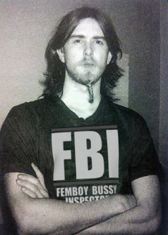 Мужчина с длинными волосами держит табличку FBI Femboy Bussy Inspector на пародийной фотографии при задержании.