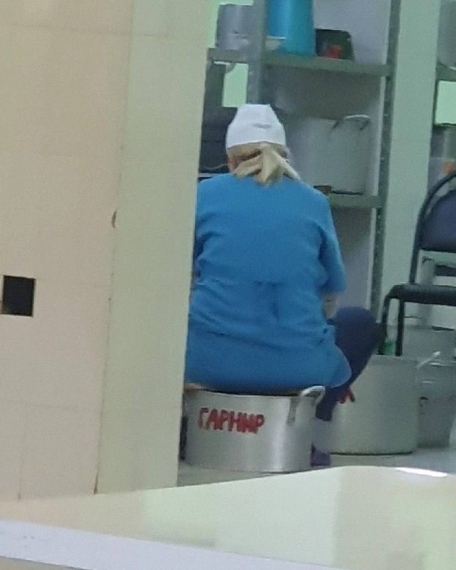 Женщина сидит на гарнире Женщина в синей униформе и белой шапочке сидит на большой металлической кастрюле с надписью «ГАРНИР».