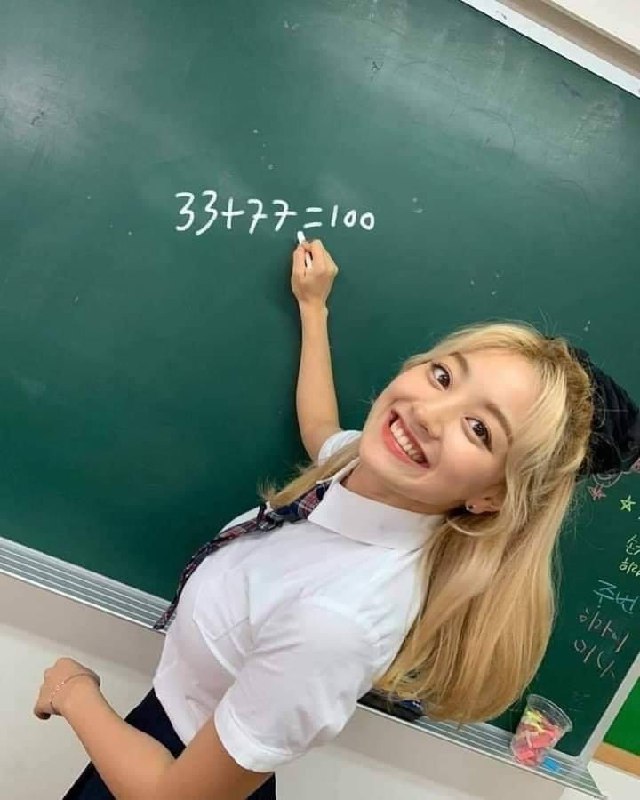 Девушка пишет 33+77=100 на доске Девушка с радостной улыбкой пишет на зеленой доске математическое выражение 33+77=100