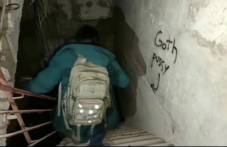 Человек спускается по лестнице в подземелье, где на стене написано "Goth pussy"