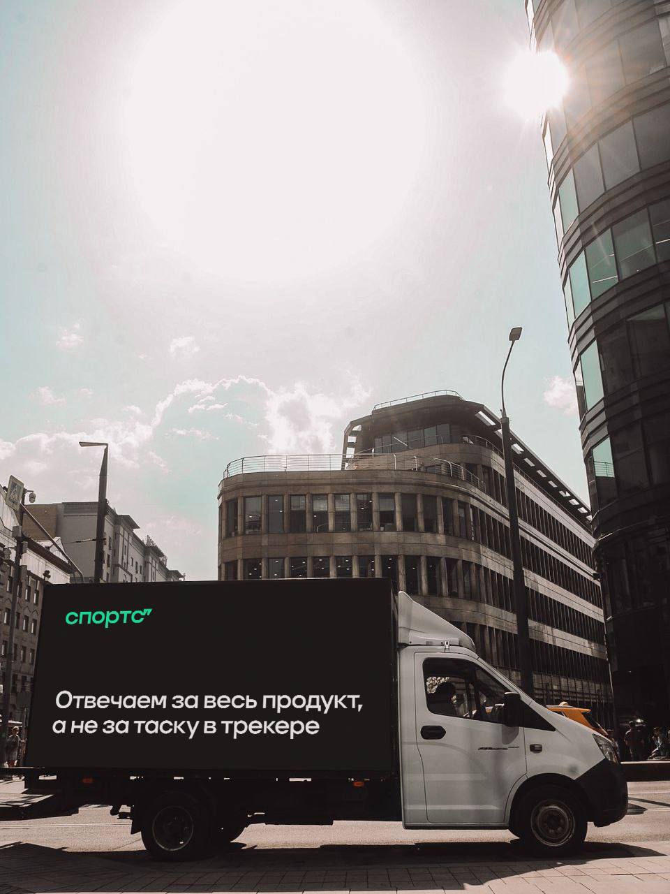 Отвечаем за весь продукт, а не за таску в трекере Грузовик с логотипом "Спортс" и надписью "Отвечаем за весь продукт, а не за таску в трекере" едет по улице города в солнечную погоду