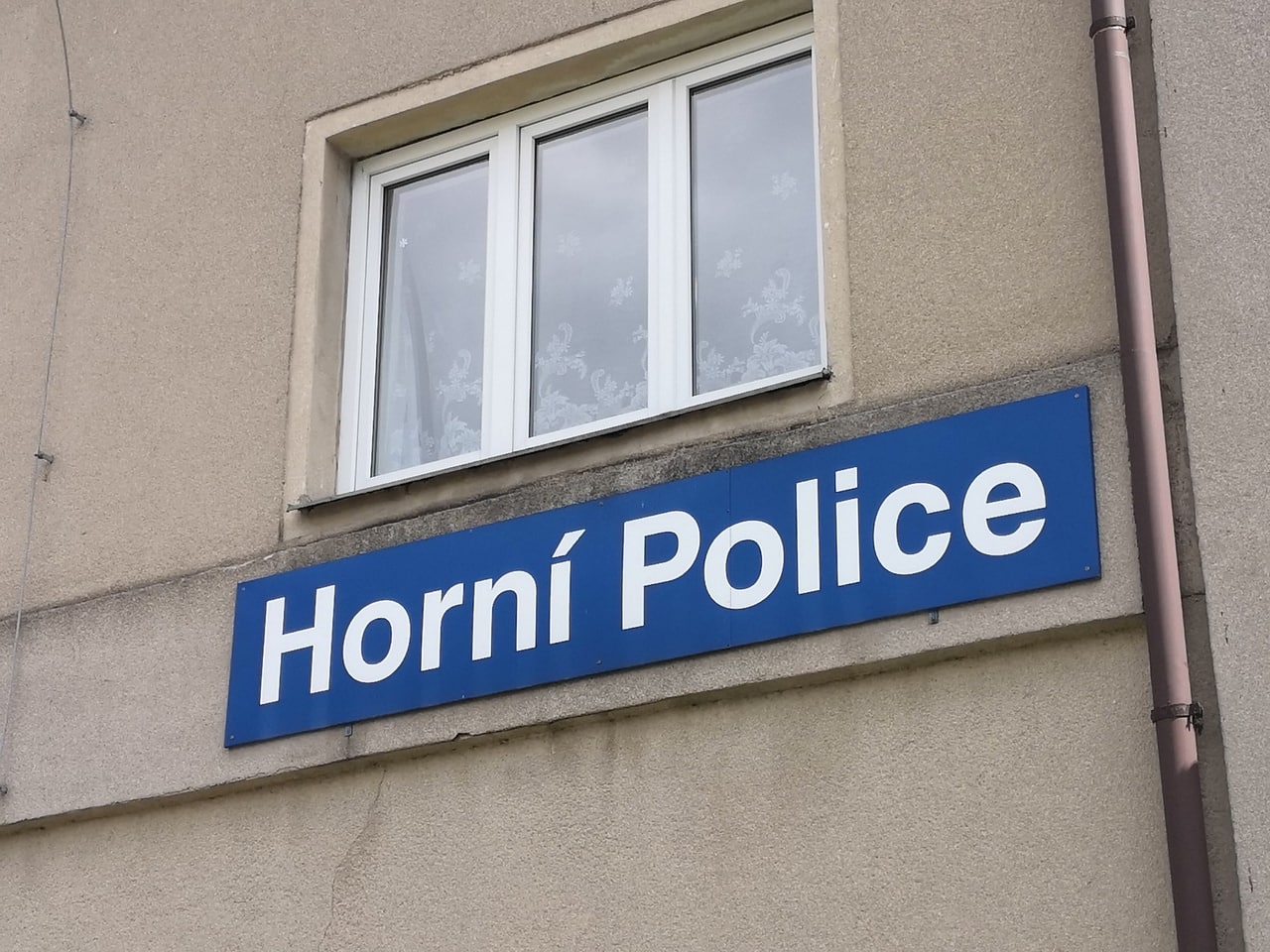 Надпись Horní Police на здании Синяя вывеска с надписью «Horní Police» на серой стене под окном