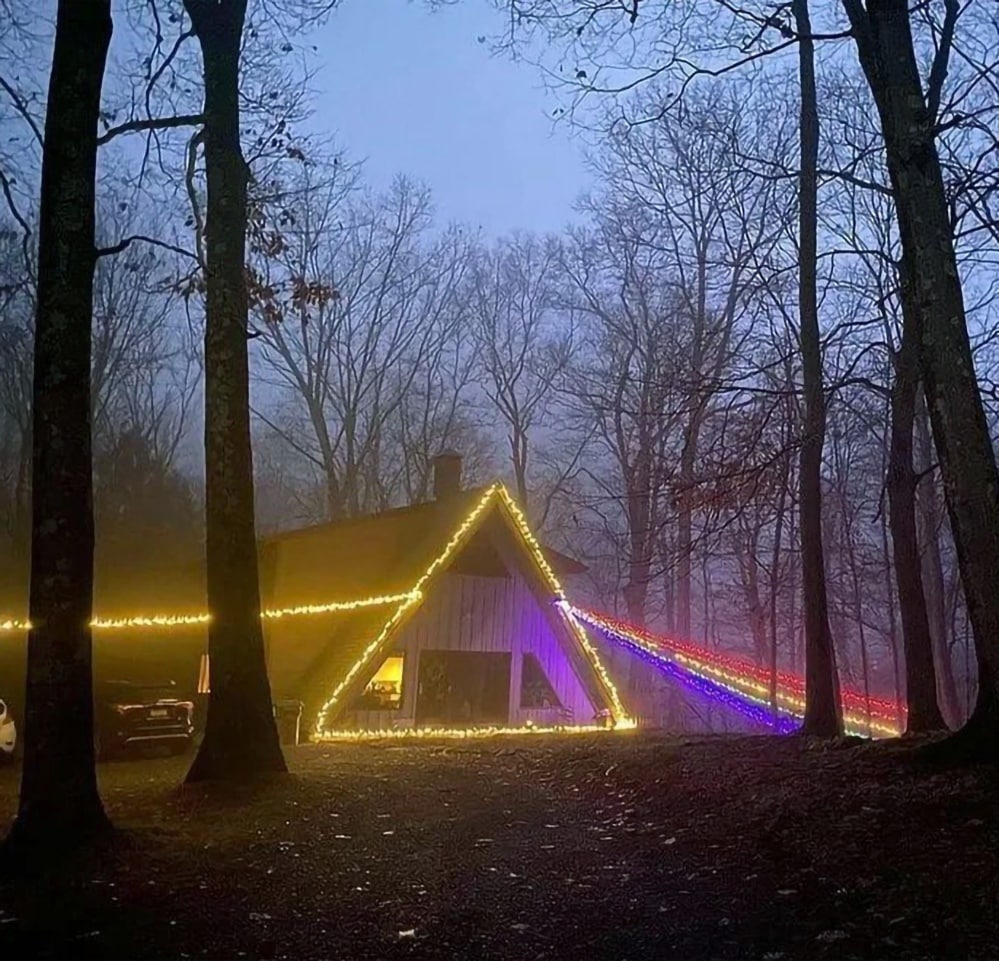 Дом в лесу с радужными огнями Pink Floyd Дом в лесу, украшенный гирляндами в стиле обложки альбома Pink Floyd The Dark Side of the Moon, с лучами света, преломляющимися в радугу.
