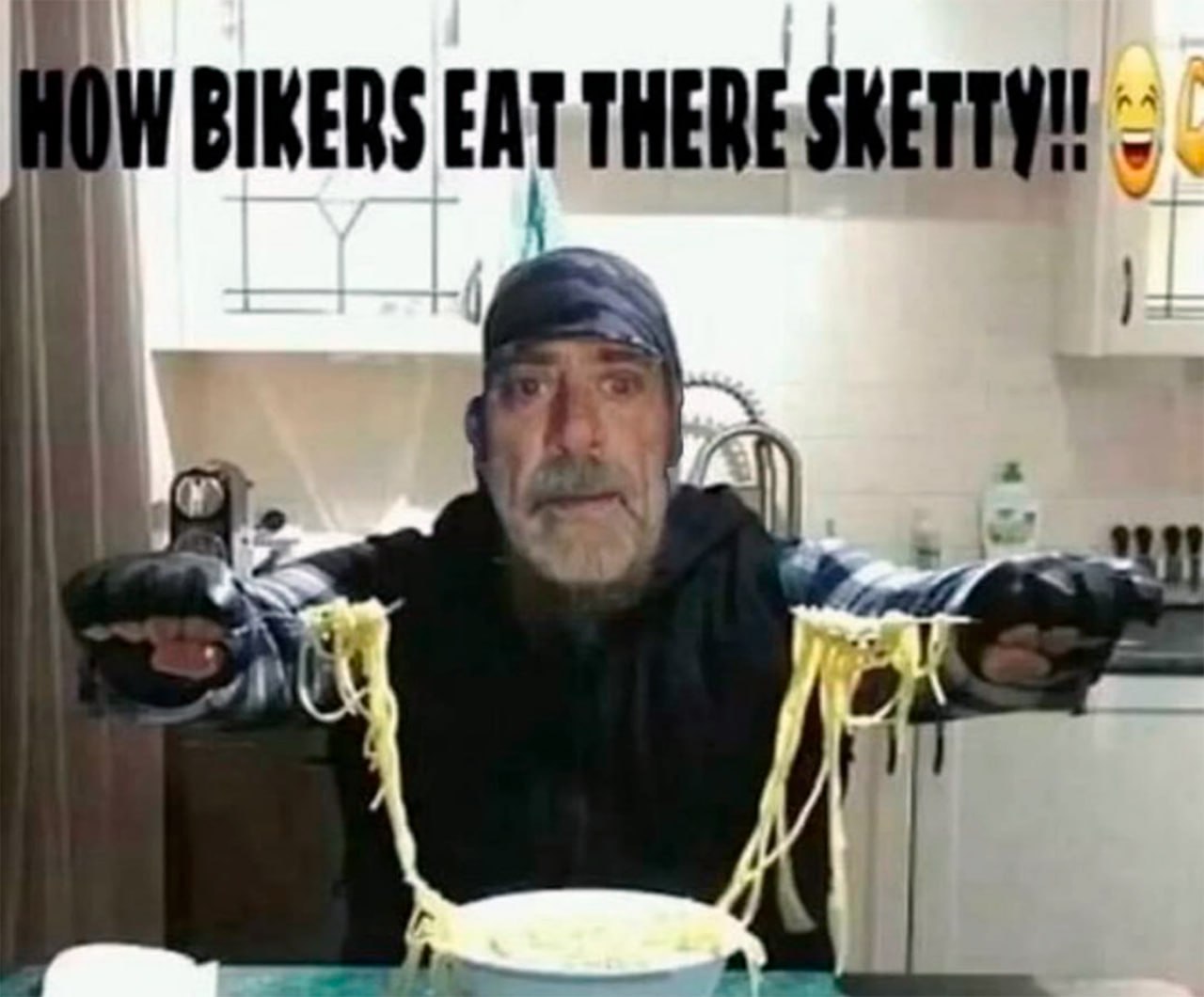 How bikers eat there sketty Мужчина в бандане ест спагетти вилками, надетыми на мотоциклетные перчатки, в комичной позе с удивлённым выражением лица.