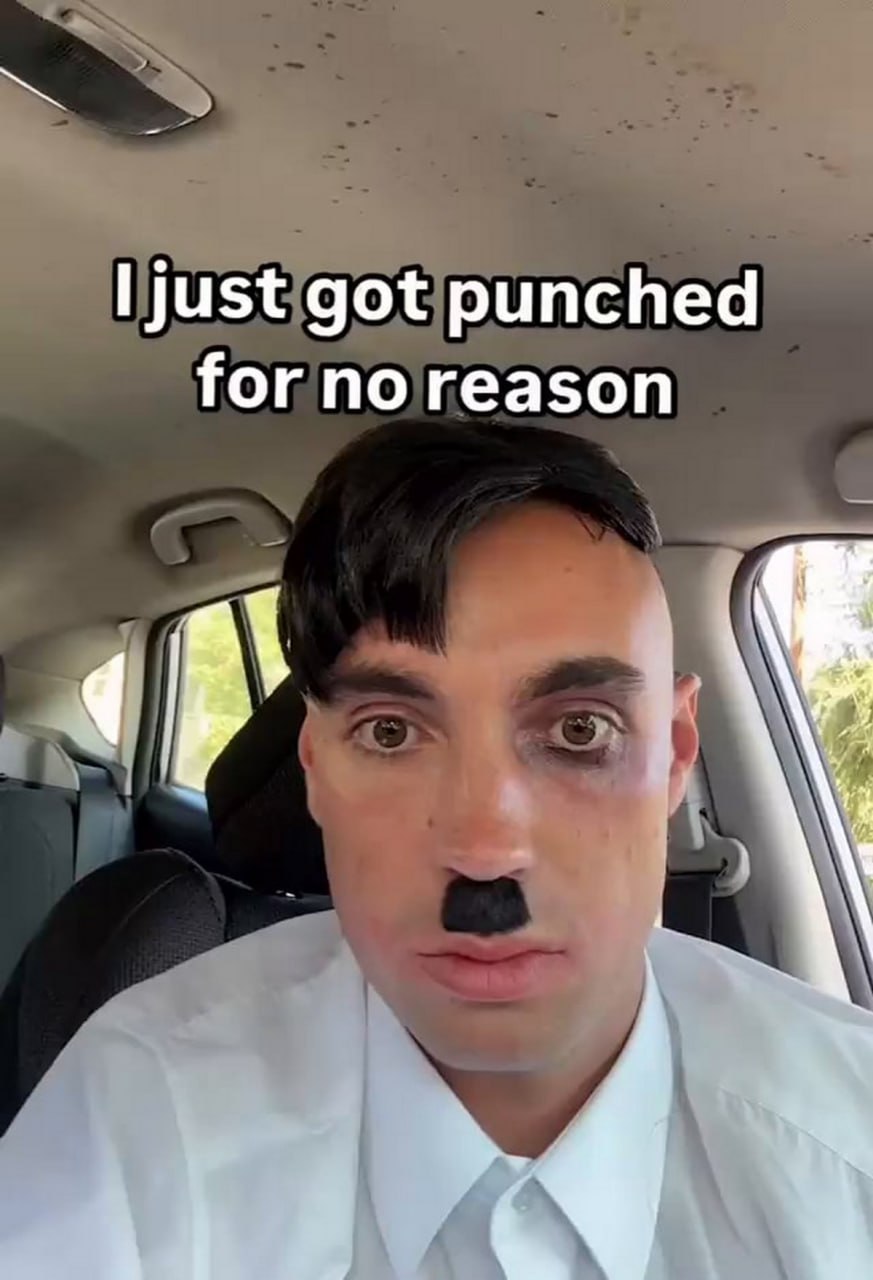 I just got punched for no reason Мужчина в костюме Гитлера с синяком под глазом и надписью «Меня только что ударили без причины»