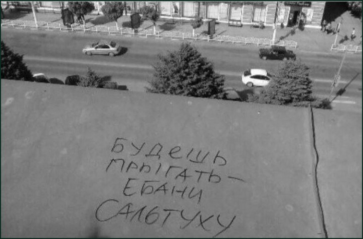 Рукописная надпись на крыше: «Будешь прыгать — ебану сальтуху» на фоне городской улицы.
