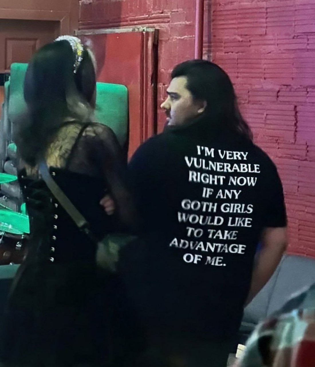 I'm very vulnerable right now if any goth girls would like to take advantage of me Мужчина в черной футболке с надписью 'I'm very vulnerable right now if any goth girls would like to take advantage of me' общается с девушкой в готическом наряде