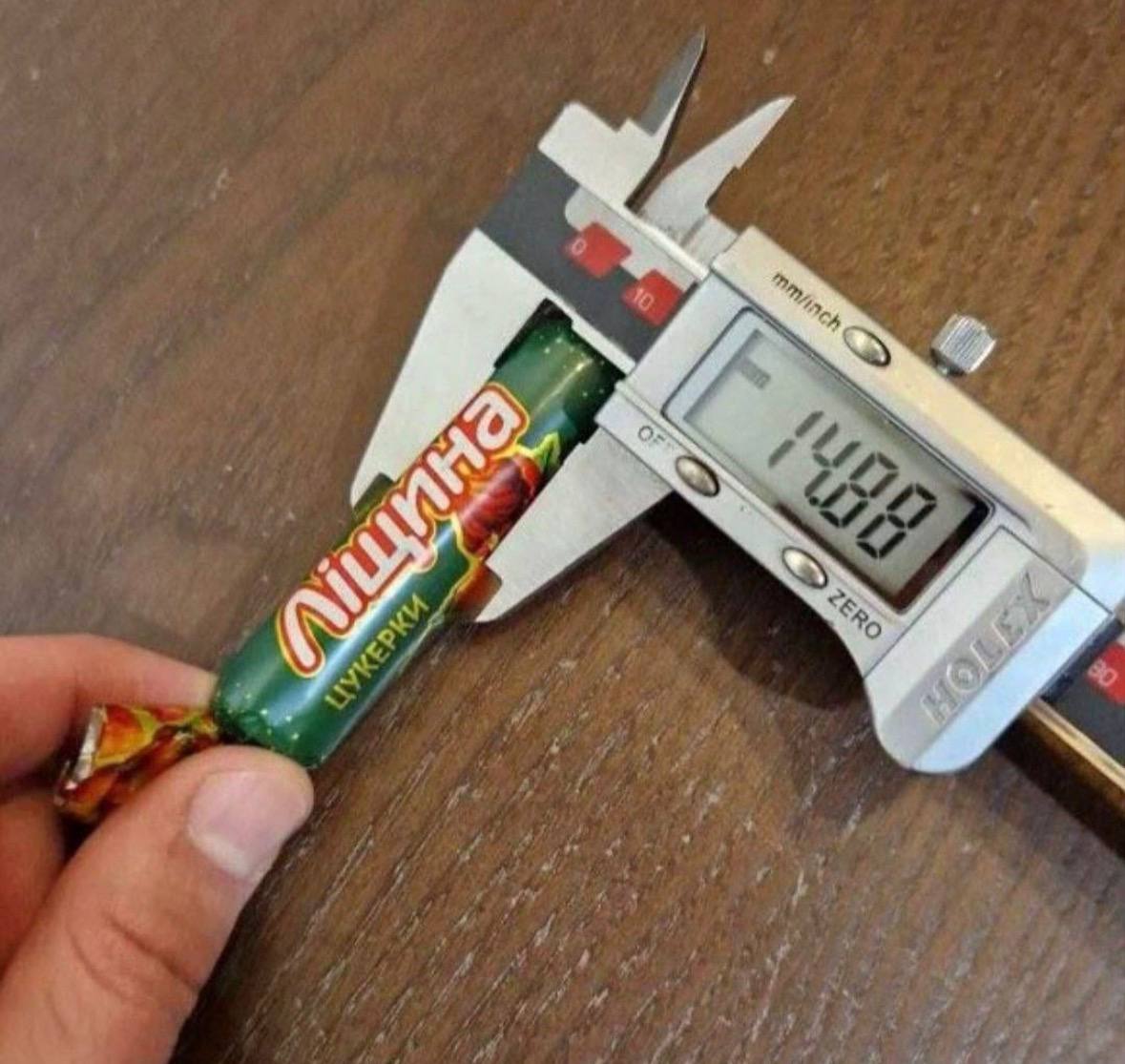 Конфета Лещина и 1488 на штангенциркуле На изображении показана конфета Лещина, которую измеряют цифровым штангенциркулем, показывающим значение 14.88 мм.