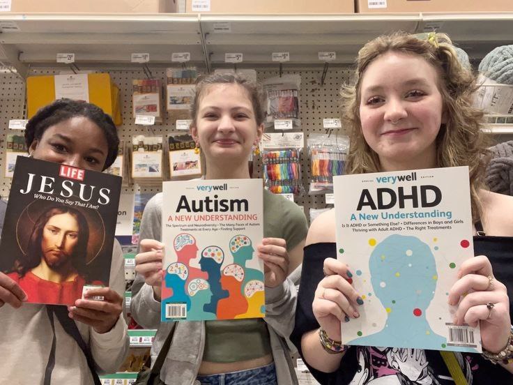 LIFE Jesus Autism ADHD Три девушки стоят в магазине, держа в руках журналы LIFE Jesus, Verywell Autism и Verywell ADHD, улыбаются и позируют для фото.