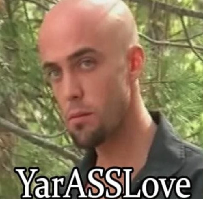 Мужчина с лысой головой и надпись YarASSLove Крупный план лысого мужчины с выражением лица, которое обычно появляется на картинках с забавными подписями. Мужчина выглядит несколько скептически или удивленно. На фоне видны зеленые листья деревьев, что указывает на природу.