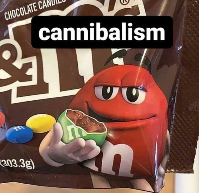 M&M's каннибализм Красный M&M's держит в руке надкусанную конфету зеленого цвета, на которой видна шоколадная начинка. Фон — упаковка из-под конфет M&M's.