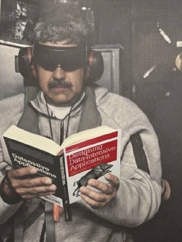 Мужчина, похожий на Мадуро, в солнцезащитных очках и наушниках читает Designing Data-Intensive Applications