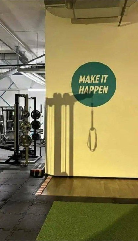 Мотивационная надпись «MAKE IT HAPPEN» на стене спортзала и забавная тень гимнастического кольца.