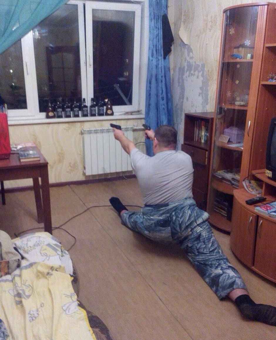 Мужчина в шпагате с двумя пистолетами Мужчина в шпагате с двумя пистолетами целится в окно с бутылками на подоконнике