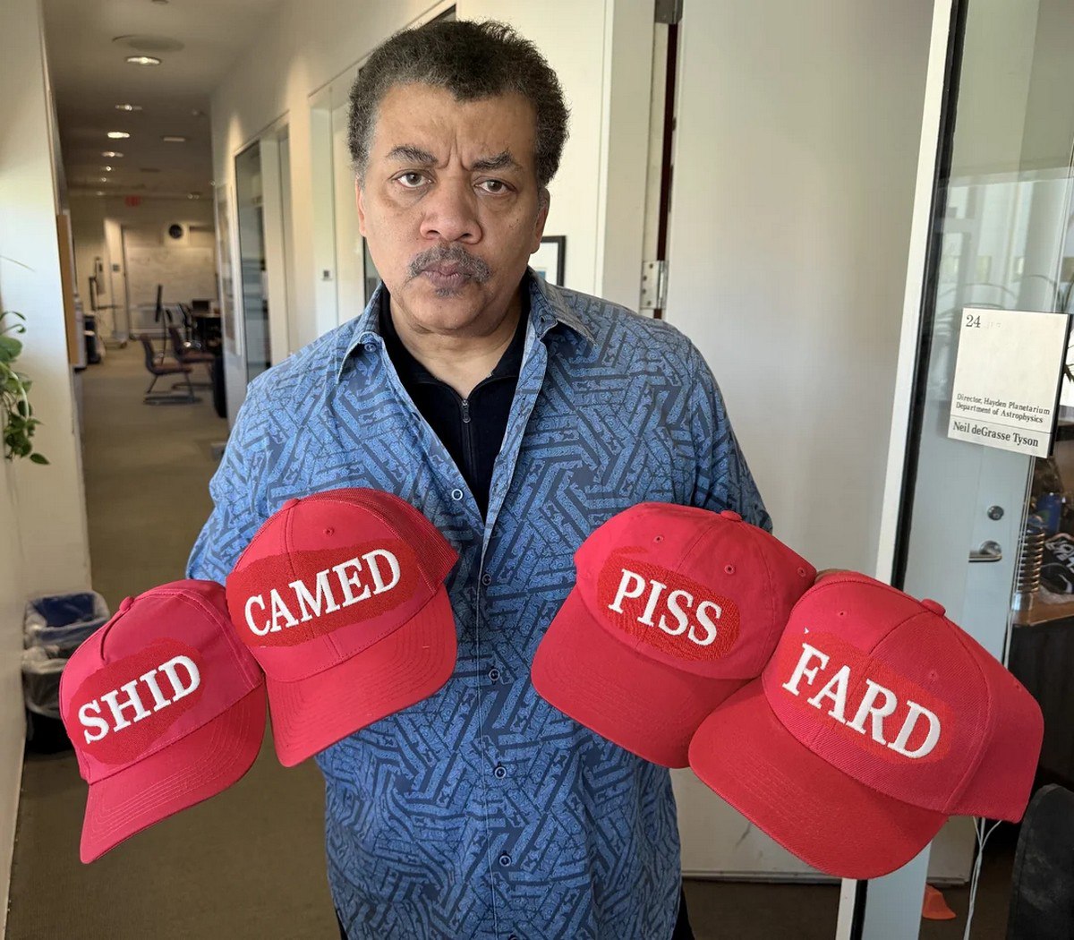 Нил Деграсс Тайсон с кепками Shid Came Fard Piss Нил Деграсс Тайсон держит четыре красные бейсболки со словами «SHID», «CAMED», «PISS» и «FARD».