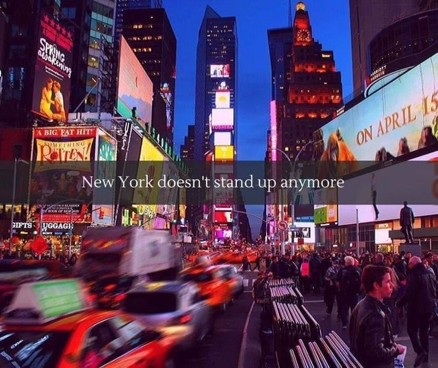 New York doesn't stand up anymore Мем с надписью «New York doesn't stand up anymore» на фоне вечерней улицы Нью-Йорка с множеством людей, машин и ярких рекламных вывесок.