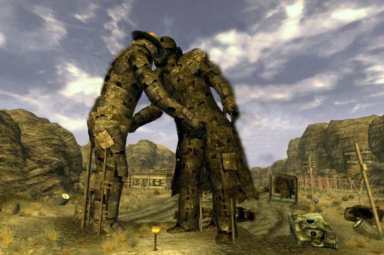 Обнимающиеся статуи из Fallout New Vegas Две гигантские статуи из ржавого металла обнимаются в пустыне, создавая ощущение заброшенности и постапокалипсиса.