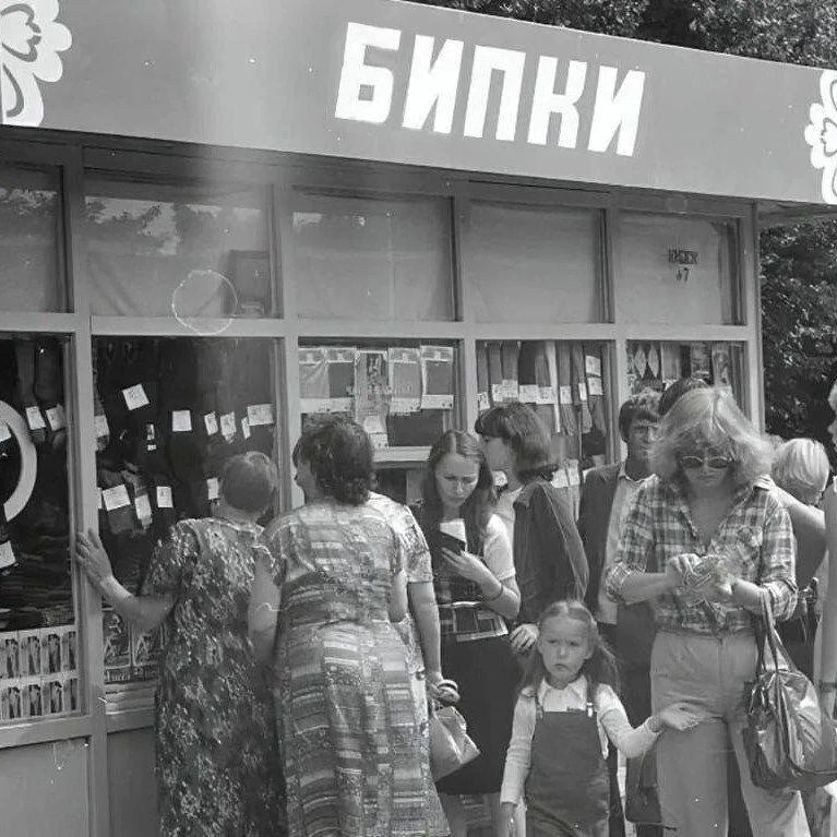 Черно-белое фото длинной очереди у книжного киоска с вывеской «БИПКИ», где люди стоят за книгами и журналами.