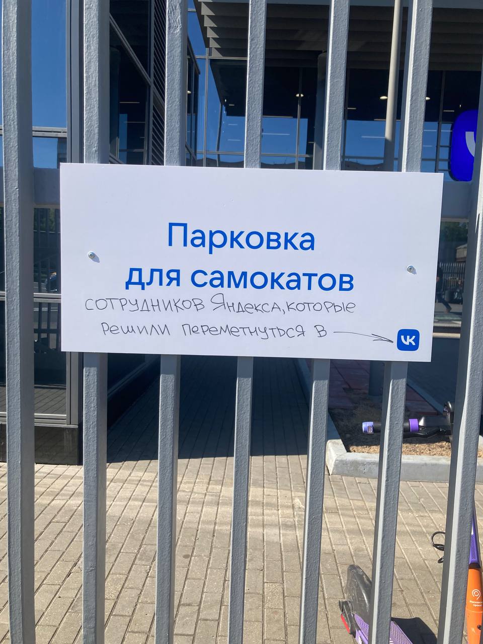 Парковка для самокатов сотрудников Яндекса, которые решили переметнуться в VK Табличка на ограде с надписью «Парковка для самокатов сотрудников Яндекса, которые решили переметнуться в VK»