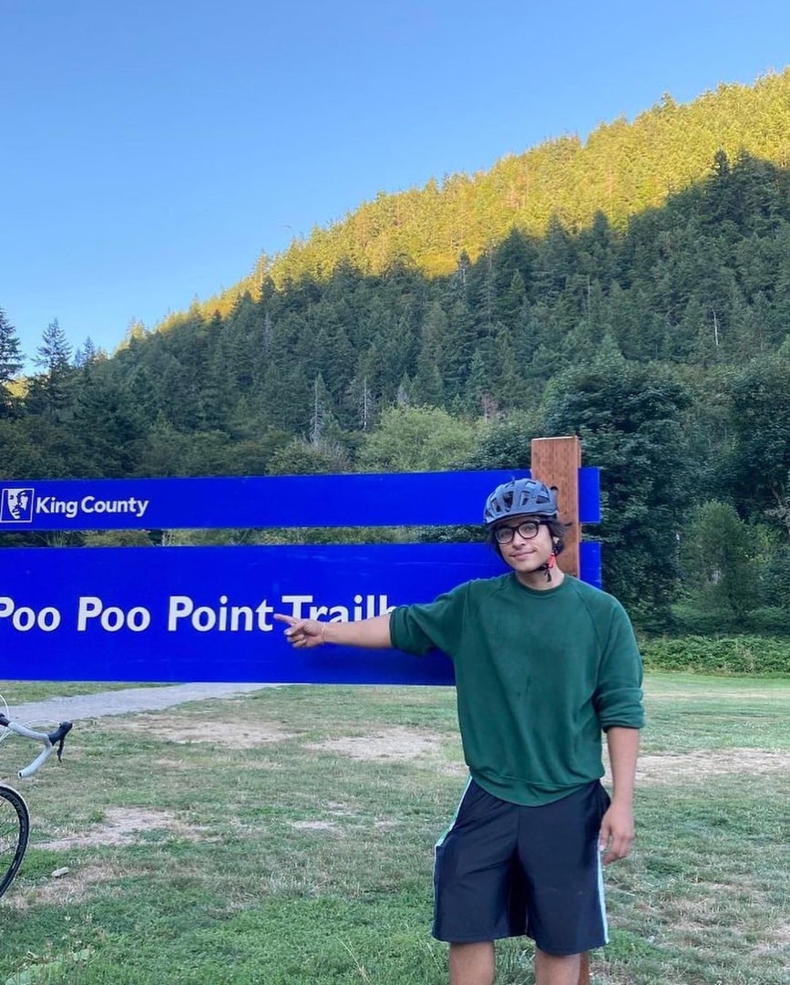 Poo Poo Point Trail Молодой человек указывает на дорожный указатель с надписью «Poo Poo Point Trail» в окружении леса.