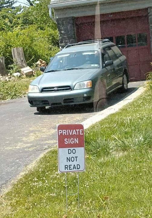 Private sign do not read Мем с табличкой Private sign do not read, стоящей на газоне у дороги к гаражу с припаркованной машиной.