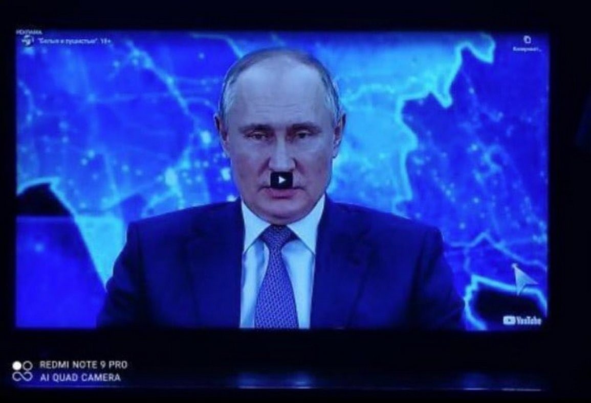 Путин с кнопкой YouTube на лице Фотография экрана с изображением Владимира Путина, на котором наложено черное окошко воспроизведения YouTube, напоминающее усы.