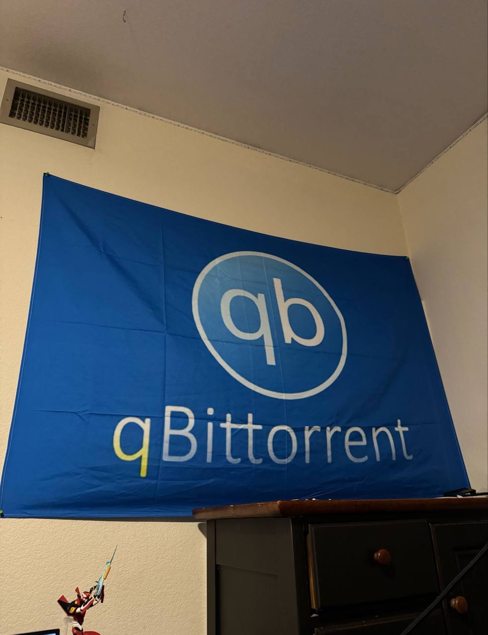 Большой синий флаг qBittorrent висит на стене над комодом в комнате.
