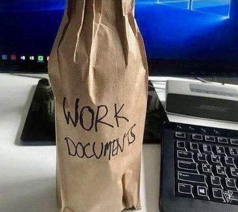 Рабочие документы в пакете Коричневый бумажный пакет с надписью "Work documents" стоит на столе рядом с ноутбуком и монитором.