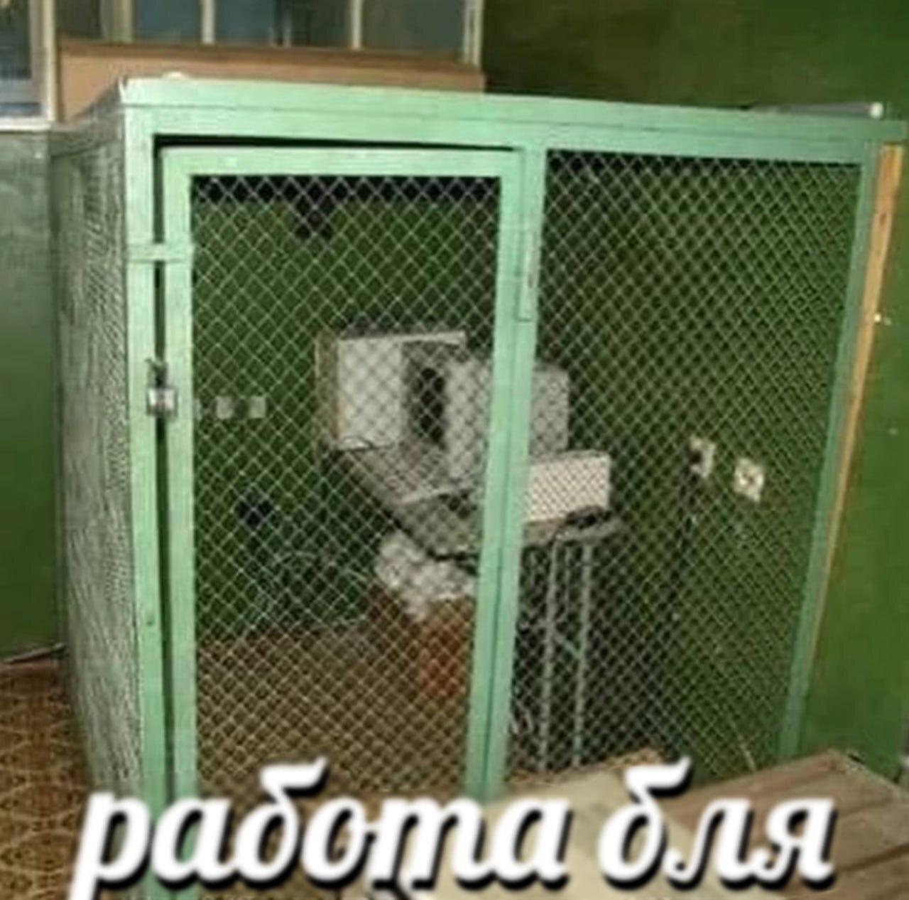 Работа бля Мем с изображением старого компьютера, помещённого в металлическую клетку, на фоне грязного помещения и надписью «работа бля» внизу.