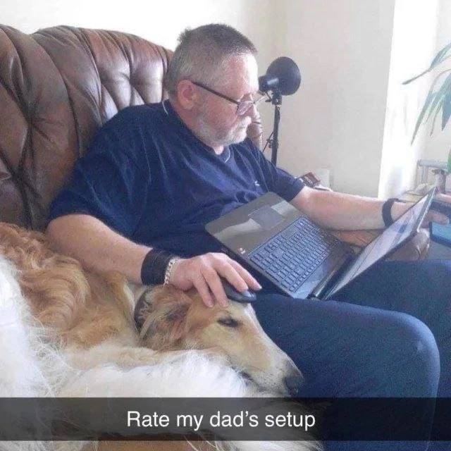 Rate my dad's setup Мужчина сидит на диване с ноутбуком на коленях и гладит собаку, лежащую рядом. Рядом стоит микрофон.