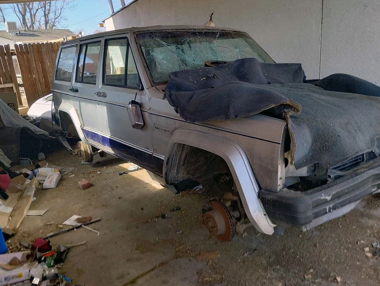 Разобранный Jeep Cherokee XJ Старый, разобранный Jeep Cherokee XJ без колес, на котором лежит черное покрывало.